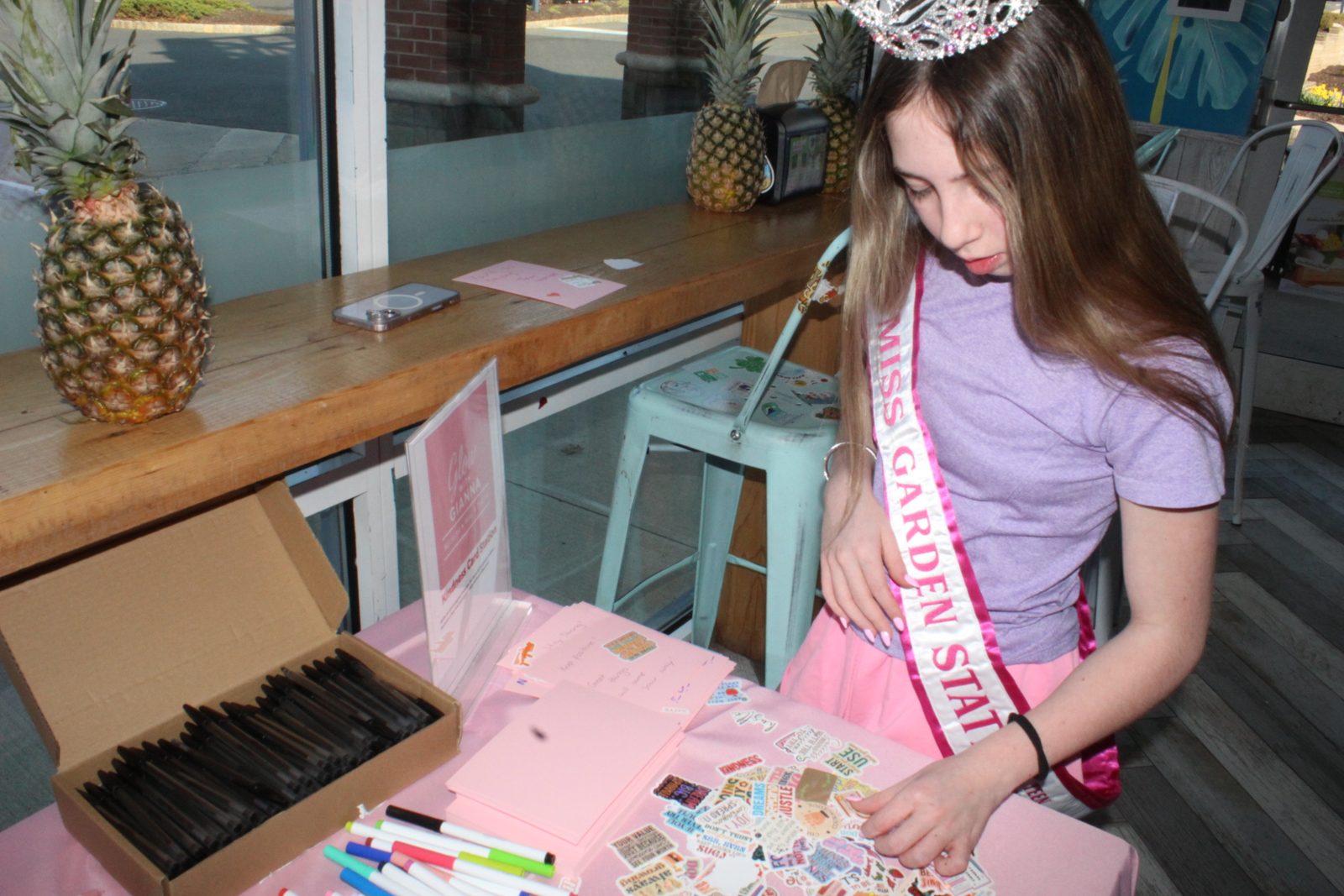 Kayla making cards at a kindness table in her sash and crown